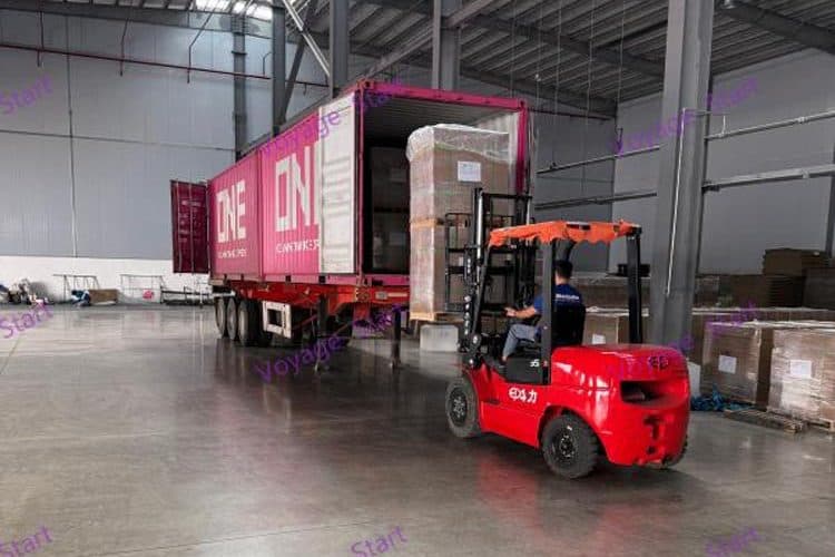 A forklift carrying a stretch-wrapped pallet into an open shipping container at the plant's loading bay.