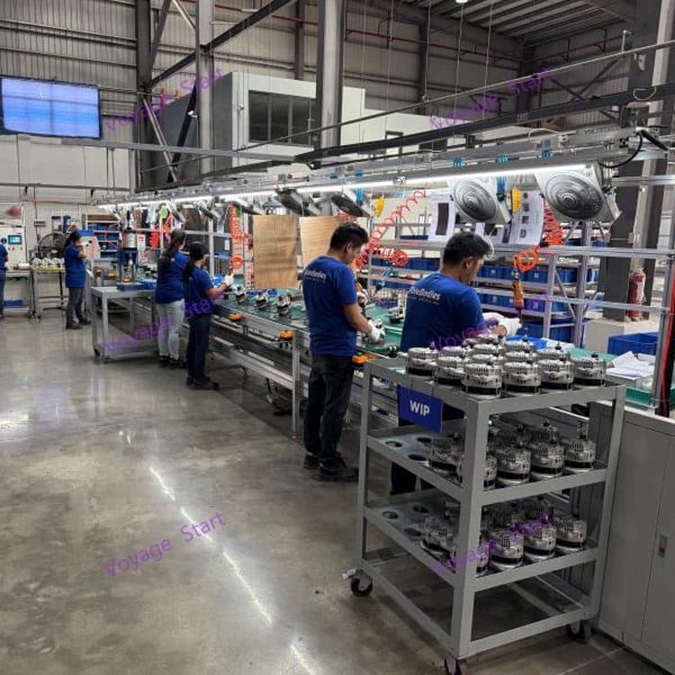 Operators working along an alternator assembly line, with a trolley of finished rotors in the foreground.