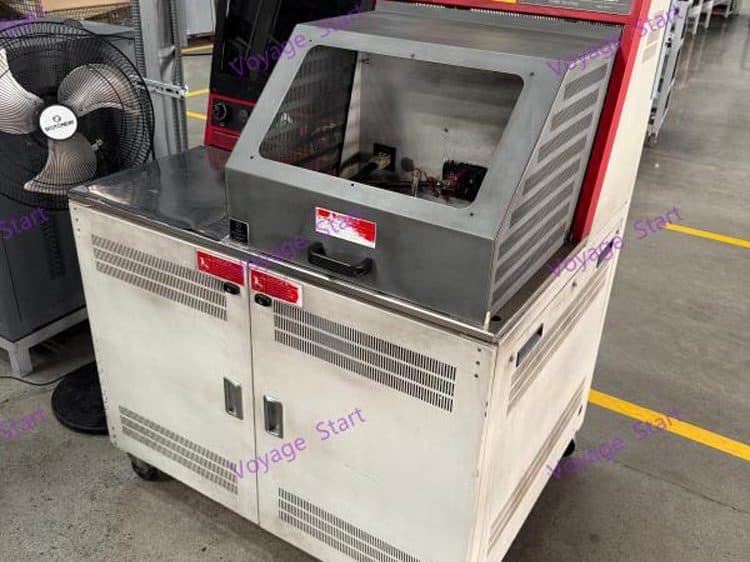 A wheeled alternator performance test stand on the production floor, its clear-window enclosure raised over the test bay.